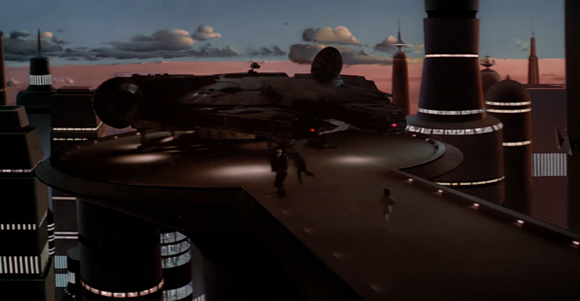 Cena do filme Star Wars exibindo pessoas correndo em uma plataforma em direção a uma nave. Ao fundo, os prédios de uma cidade e o céu azul-claro com nuvens.