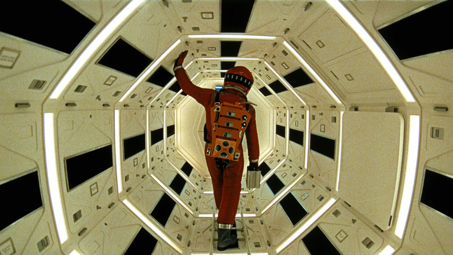 Imagem de uma pessoa com roupa de astronauta vermelha vista de costas andando em uma nave espacial branca iluminada por luzes brancas.