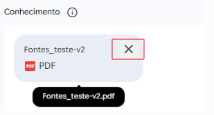 Captura de tela de uma interface de usuário exibindo um arquivo PDF anexado sob o título "Conhecimento". O arquivo se chama "Fontes_teste-v2" e exibe um pequeno ícone vermelho de PDF. À direita do nome do arquivo, há um botão com um ícone de "X" destacado por um retângulo vermelho, indicando a opção de excluir o anexo. Abaixo do card, um balão preto (tooltip) mostra o nome completo do arquivo: "Fontes_teste-v2.pdf".