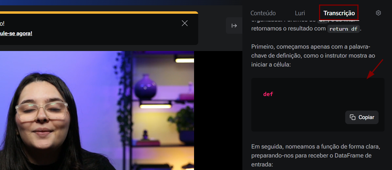 Captura de tela de uma video aula na plataforma Alura. Do lado esquerdo, há a gravação de um vídeo mostrando o rosto em close de uma mulher. Do lado direito, há uma barra lateral de navegação com as abas "Conteúdo", "Luri" e "Transcrição", sendo que "Transcrição" está destacada com um retângulo vermelho. Abaixo, o texto em português explica conceitos de programação Python, mostrando um bloco de código preto com a palavra-chave "def" em rosa e um botão "Copiar" no canto inferior direito. Uma seta vermelha aponta para esse bloco de código.