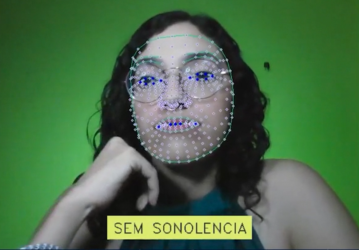 Uma janela de vídeo é aberta na tela, com a instrutora na imagem. Há uma série de pontos faciais brancos mapeando seu rosto. Primeiro, ela está sonolenta e a música é lenta. Em seguida, há um aviso sonoro pontual e mais alto, momento em que desperta e aparece a legenda "sem sonolência". Não há fala durante o vídeo.