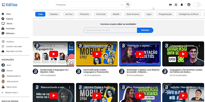 Interface do VidFlow, plataforma de compartilhamento de vídeo, cujas cores predominantemente são azul para destaques e branco para o fundo. Na área principal, há várias miniaturas de vídeos, com títulos abaixo de si. As miniaturas apresentam imagens estáticas e um botão de reprodução vermelho no centro. Acima da área principal, há um espaço de para inscrição com o texto 'Inscreva-se para saber as novidades!', um campo para inserção de e-mail e o botão 'Inscrever'. Acima do espaço da inscrição, existe uma barra horizontal com botões de categorias de navegação, tais como 'Tudo', 'Debates', 'Ao Vivo', 'Podcasts', 'Front-end', 'Mobile', 'Data Science', 'Apps', 'Programação' e 'Inteligência Artificial'. Acima das categorias, há um campo de pesquisa de vídeos, com um botão de lupa à direita. Na lateral superior direita, há quatro botões comuns, com ícones de câmera de vídeo, grade, sino e o avatar da conta, além de um botão de alternância desativado. Na lateral esquerda, ocupando o comprimento da tela, há uma barra de opções de menu, dividida em quatro seções: na superior, encontram-se a logo do VidFlow, além das opções de menu 'Início', 'Explorar', 'Shorts', 'Inscrições' e 'Biblioteca'. Abaixo dela, há as seção com as opções 'Histórico', 'Assistir mais tarde' e 'Marcados com like'. Na seção seguinte, há o título 'INSCRIÇÕES' e uma lista de canais específicos, abaixo dos quais há a opção 'Mostrar mais 2', indicando mais canais nessa lista. Já na seção inferior, há o texto 'MAIS DA PÁGINA', indicando mais conteúdo