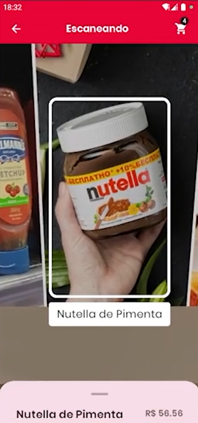 ALT: Tela de escaneamento do aplicativo, mostrando a imagem da mão de uma pessoa segurando um pote de Nutella, contornada por um retângulo branco. Abaixo deste, um retângulo branco com a descrição 'Nutella de Pimenta'. Na parte inferior da tela, uma aba rosa-claro com o mesmo nome de produto e o preço R$ 56,56.