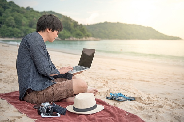 Hombre sentado en la arena trabajando desde la playa, durante un atardecer